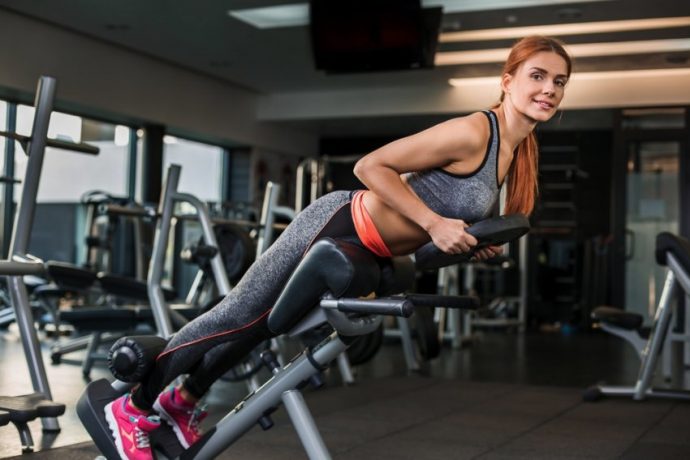 Девушка выполняет гиперэкстензию с отягощением